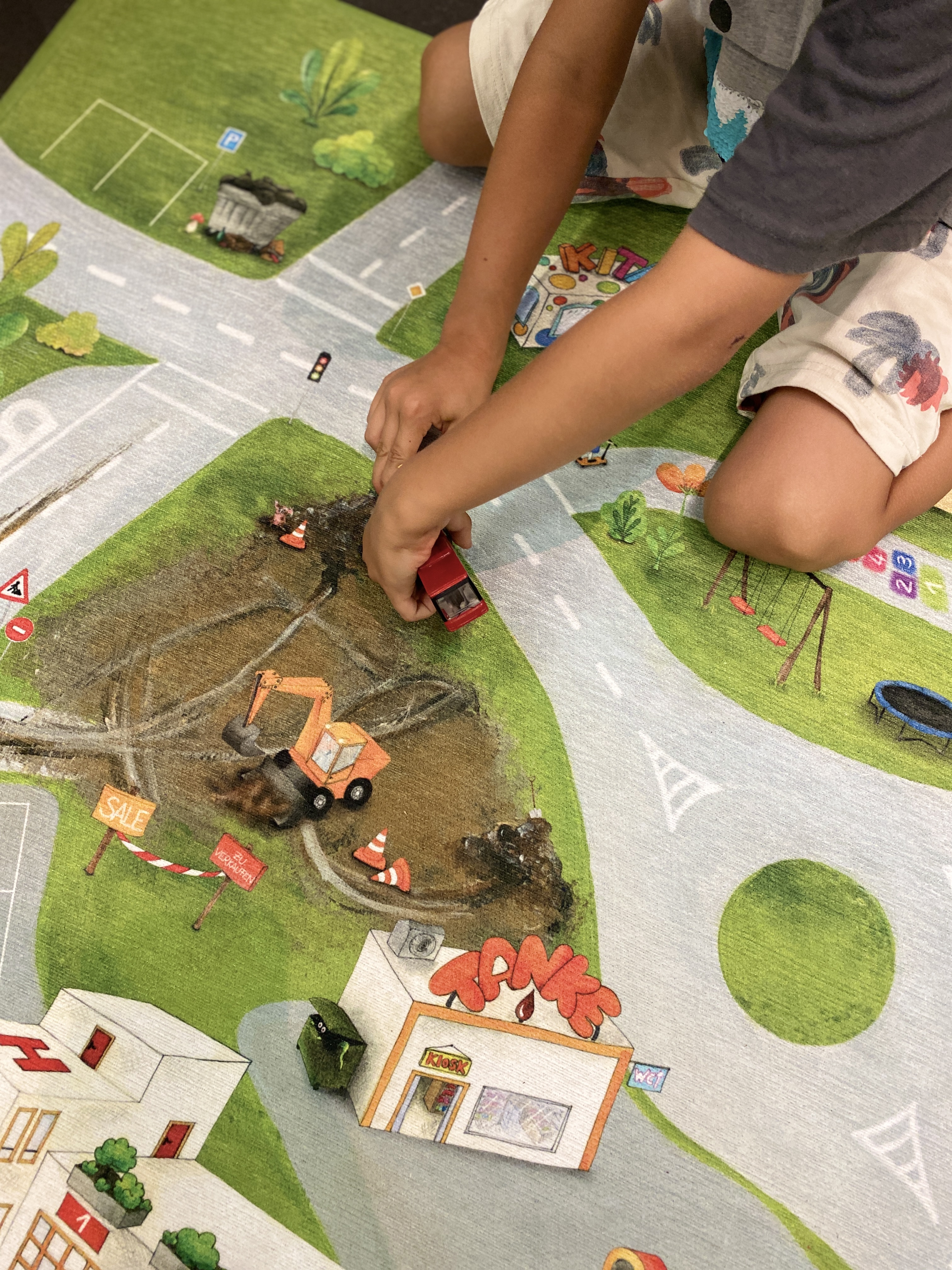 Kind spielt auf Spielteppich mit Spielzeugautos